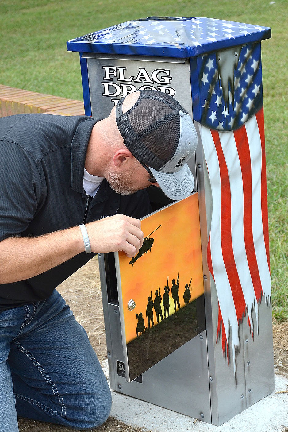 Veteran John Vincent affixes the flag drop box to bolts in the concrete in front of the Veterans Memorial downtown Friday.