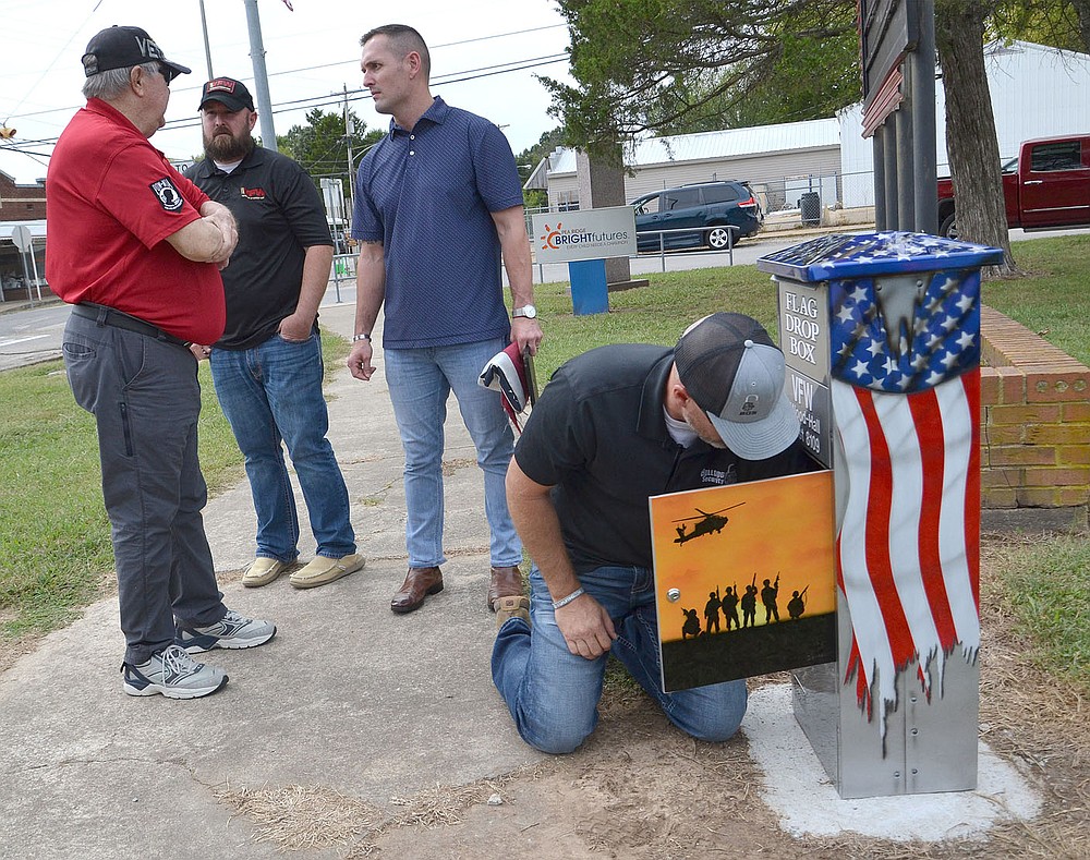 Veterans Jerry Burton, Terry Thurman and Braxton Hurst visit while fellow veteran John Vincent affixes the flag drop box to bolts in the concrete in front of the Veterans Memorial downtown Friday.