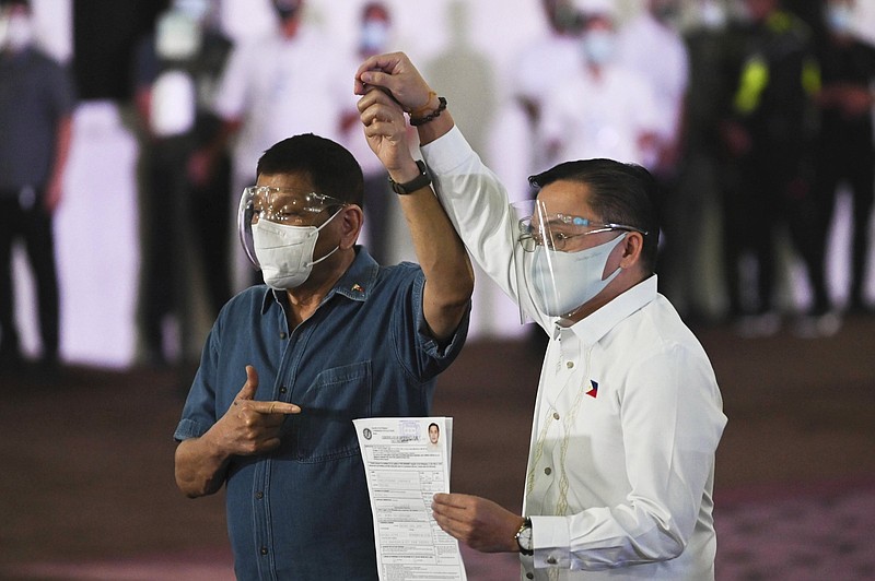 Philippine President Rodrigo Duterte, left, raises the hand of Sen. Bong Go who has filed his certificate of candidacy for vice-president during next year's elections before the Commission on Elections at the Sofitel Harbor Garden Tent in Metropolitan Manila, Philippines on Saturday, Oct. 2, 2021. Duterte says he is backing out of an announced plan to run for vice president in next year's elections and will retire from politics after his term ends. (Lisa Marie David/Pool Photo via AP)