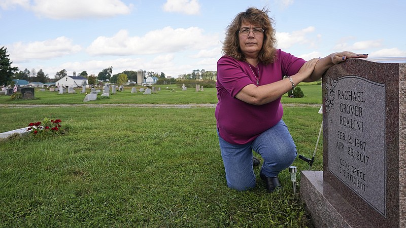 Sharon Grover rests her hands on the gravestone for her daughter, Rachael, Tuesday, Sept. 28, 2021, at Fairview Cemetery in Mesopotamia, Ohio. Grover believes her daughter started using prescription painkillers around 2013 but missed any signs of her addiction as her daughter, the oldest of five children, remained distanced.  (AP Photo/Tony Dejak)