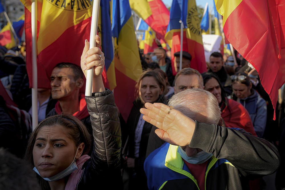 Un bărbat își acoperă fața de soare în timp ce oamenii fluturează steaguri în timpul unui protest antiguvernamental organizat de Alianța de extremă dreapta pentru Unitatea Românilor sau AUR, la București, România, sâmbătă, 2 octombrie 2021. Mii de oameni au participat la străzile cerând demisia guvernului, întrucât România a raportat 12.590 de noi infecții cu COVID-19 în ultimele 24 de ore, cel mai mare număr zilnic înregistrat de la începutul pandemiei de coronavirus.  (AP Photo/Vadim Ghirda)