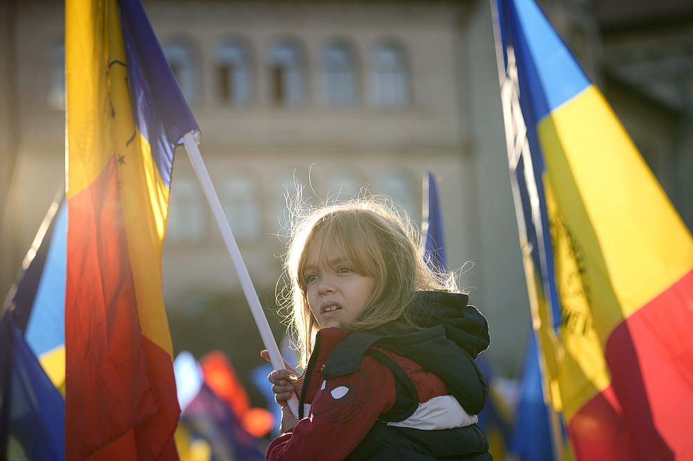 O fetiță flutură un steag în timpul unei demonstrații antiguvernamentale și anti-restricții organizată de Alianța de extremă dreapta pentru Unitatea Românilor sau AUR, la București, România, sâmbătă, 2 octombrie 2021. Mii de oameni au ieșit în stradă cerând demisia guvernului deoarece România a raportat 12.590 de noi infecții cu COVID-19 în ultimele 24 de ore, cel mai mare număr zilnic înregistrat de la începutul pandemiei.  (AP Photo/Vadim Ghirda)