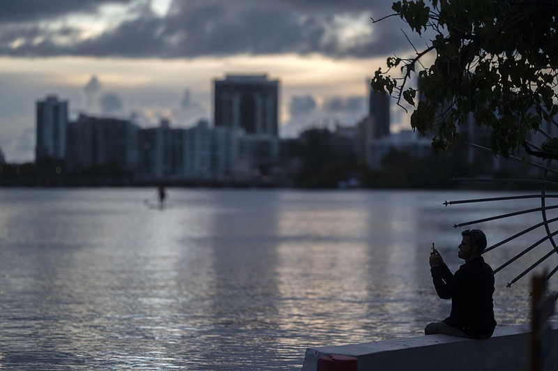 A man takes pictures with his cellphone on the banks of the Condado lagoon, where multiple selective blackouts have been recorded in the past days, in San Juan, Puerto Rico, Thursday, Sept. 30, 2021. Power outages across the island have surged in recent weeks, with some lasting up to several days. (AP Photo/Carlos Giusti)