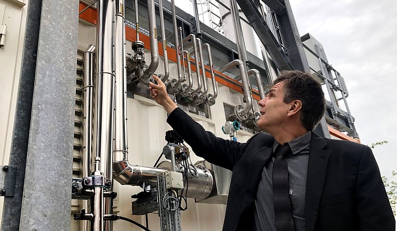 Dietrich Brockhagen, Executive Director of Atmosfair, points on pipes of the system that brings hydrogen and carbon into the facility that mix them and produce e-fuel at the 'Atmosfair' synthetic kerosene plant in Werlte, Germany, Monday, Oct. 4, 2021. German officials are unveiling a facility in Werlte, near Germany's northwestern border with the Netherlands, what they say will be the world's first commercial plant for making synthetic kerosene as part of an effort to reduce the climate impact of flying. (AP Photo/Aleksandar Furtula)