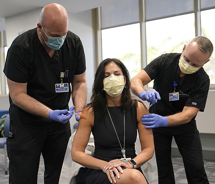 Dr. Lilian Abbo, center, receives a flu vaccine from Nicholas Torres, left, and a Pfizer COVID-19 booster shot from Douglas Houghton, right, at Jackson Memorial Hospital Tuesday, Oct. 5, 2021, in Miami. According to the Centers for Disease Control and Prevention it is safe to get your COVID-19 vaccine and flu vaccine at the same time. The COVID-19 booster is now available to those over 65 and to workers whose jobs put them at high risk of exposure. (AP Photo/Lynne Sladky)