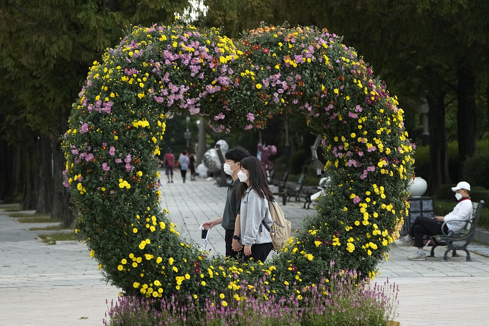 A couple wearing face masks as a precaution against the coronavirus passes by a heart-shaped chrysanthemum flower arrangement at a park in Goyang, South Korea, Tuesday, Oct. 5, 2021. (AP Photo/Ahn Young-joon)