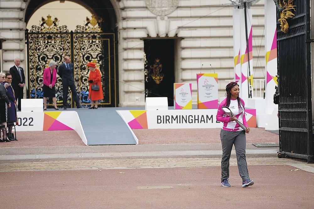 Baton bearer Britain's Kadeena Cox, who won two gold medals at the Rio 2016 Paralympic Games, walks away with the baton after receiving it from Britain's Queen Elizabeth II, on the stage in the background, at the Birmingham 2022 Commonwealth Games Queen's Baton Relay event outside Buckingham Palace in London, Thursday, Oct. 7, 2021. The city of Birmingham in England will host the 2022 Commonwealth Games. (AP Photo/Matt Dunham)