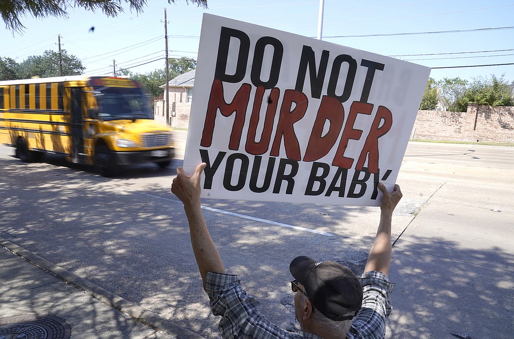 David Trujillo holds a sign as a school bus drives by on the street in front of a building housing an abortion provider in Dallas, Thursday, Oct. 7, 2021. A federal judge has ordered Texas to suspend a new law that has banned most abortions in the state since September. The order Wednesday by U.S. District Judge Robert Pitman freezes for now the strict abortion law known as Senate Bill 8. (AP Photo/LM Otero)