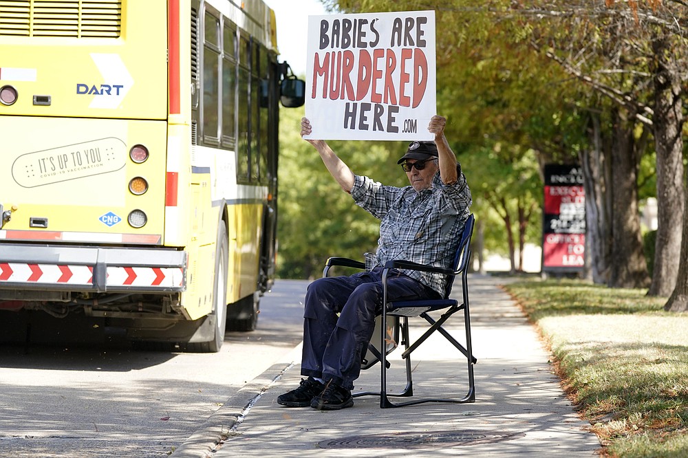 David Trujillo holds a sign a bus drives by on the street in front of a building housing an abortion provider in Dallas, Thursday, Oct. 7, 2021. A federal judge has ordered Texas to suspend a new law that has banned most abortions in the state since September. The order Wednesday by U.S. District Judge Robert Pitman freezes for now the strict abortion law known as Senate Bill 8. (AP Photo/LM Otero)