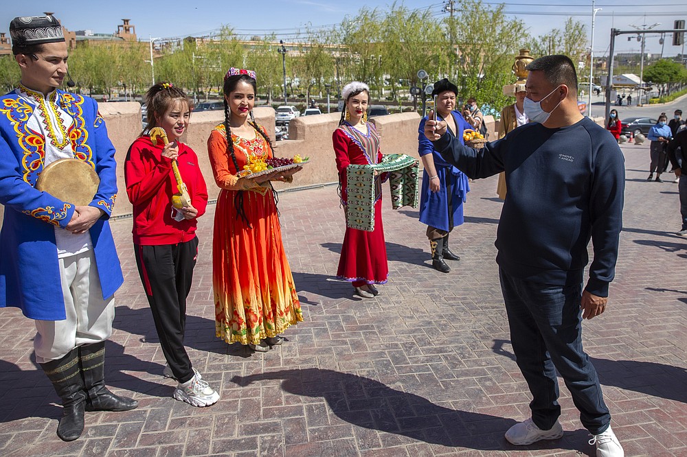 A tourist snaps pictures of Uyghur performers at the front gate of the remodeled city center of Kashgar in China's far west Xinjiang region, during the welcome ceremony of a state tour for foreign media on April 19, 2021. Four years after Beijing's brutal crackdown on largely Muslim minorities native to Xinjiang, Chinese authorities are dialing back the region's high-tech police state and stepping up tourism. But even as a sense of normality returns, fear remains, hidden but pervasive. (AP Photo/Mark Schiefelbein)
