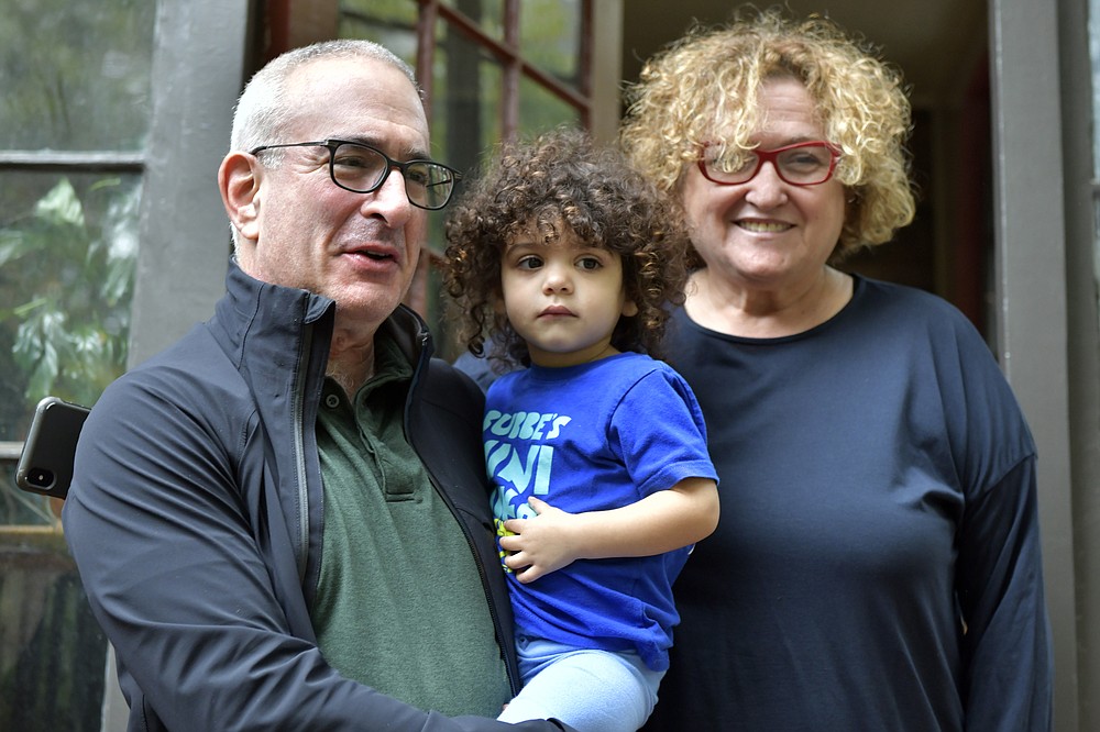 Winner of the Nobel prize for economics Joshua Angrist speaks to a reporter with his granddaughter Bella, and wife Mira Angrist, a professor of Hebrew at Boston University, from his home Monday, Oct. 11, 2021, in Brookline, Mass. Angrist, a professor at the Massachusetts Institute of Technology, shared the prize with David Card of the University of California at Berkeley and Guido Imbens from Stanford University. Angrist and Imbens won for their work on methods that allow economists to draw conclusions about cause and effect where studies cannot be carried out according to strict scientific methods. (AP Photo/Josh Reynolds)