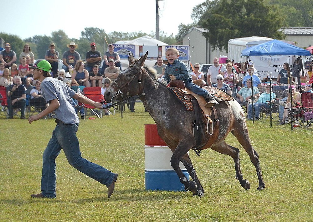 A small boy rides the mule through the barrel race while being led around the course.