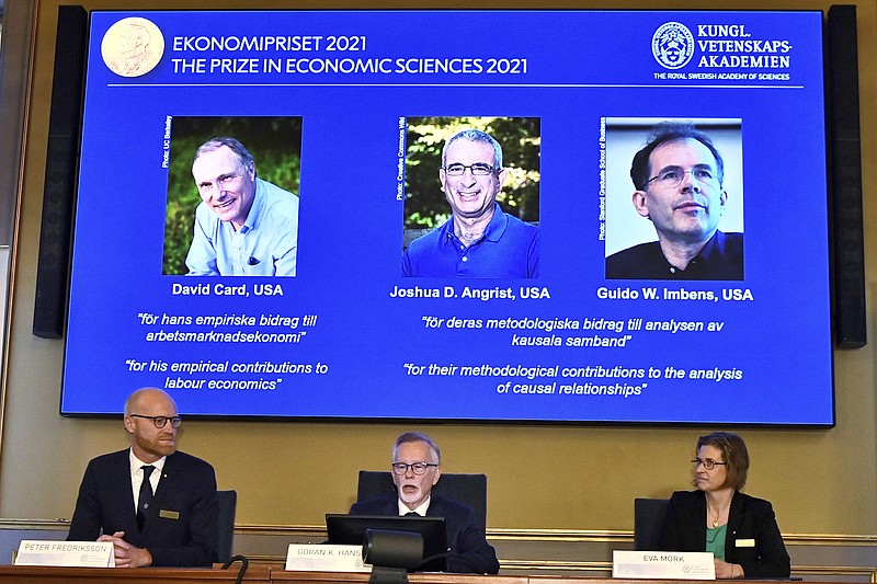 Permanent Secretary of the Royal Swedish Academy of Sciences Goran K Hansson, center, announces the 2021 Nobel prize for economics, flanked by members of the Royal Swedish Academy of Sciences Peter Fredriksson, left, and Eva Mork, during a press conference at the Royal Swedish Academy of Sciences, in Stockholm, Sweden, Monday, Oct. 11, 2021. From left on the screen above are the winners David Card of the University of California at Berkeley; Joshua Angrist from the Massachusetts Institute of Technology; and Guido Imbens from Stanford University.  (Claudio Bresciani/TT via AP)