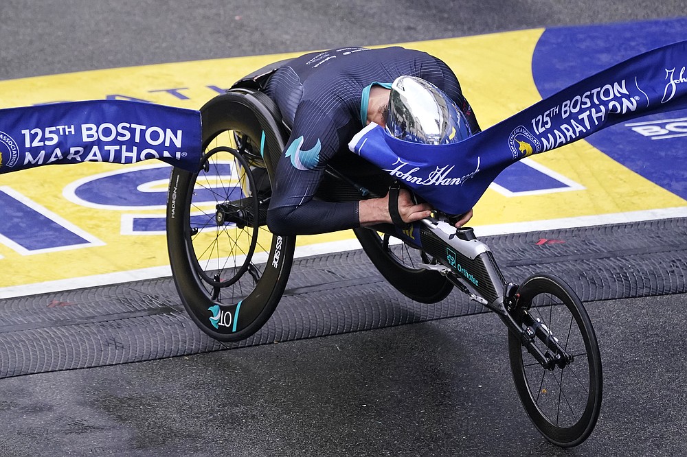Marcel Hug, of Switzerland, breaks the finish line with his helmet to win the men's wheelchair division at the Boston Marathon in Boston, Monday, Oct. 11, 2021. (AP Photo/Charles Krupa)