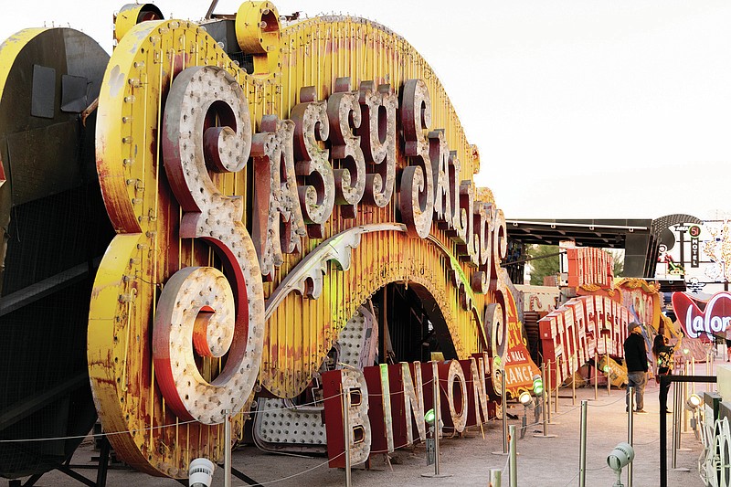 Visitors are dwarfed by the Sassy Sally's sign at the Neon Museum, Wednesday, Sept. 29, 2021, in Las Vegas. The Neon Museum will start offering guided tours in Spanish. (Yasmina Chavez/Las Vegas Sun via AP)