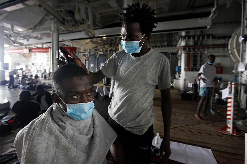 An African migrant barber shaves a mans head abroad Geo Barents after they were rescued in the Mediterranean Sea off Libya, Monday, Sept. 27, 2021. Migrants rescued say that they were tortured and their families extorted for ransoms in Libya’s detention centers. Their accounts to The Associated Press come as a report commissioned by the United Nations said last week that “crimes against humanity have been committed,” against migrants intercepted at sea and turned over to Libya’s detention centers. (AP Photo/Ahmed Hatem)