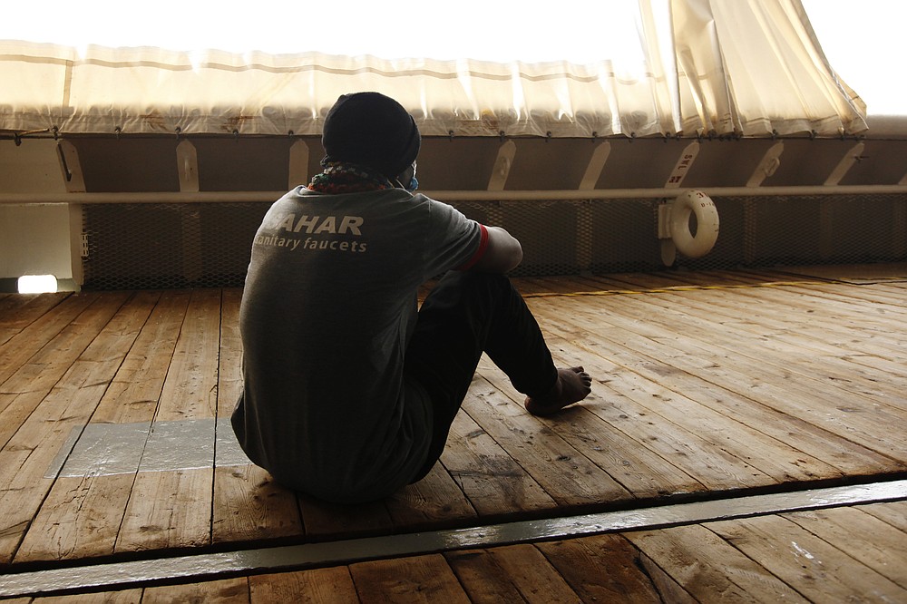 Guinean migrant Osman Touré sits on the deck of the rescue vessel Geo Barents waiting for his disembarkation after being rescued from the central Mediterranean Sea off Libya, at the port of Augusta, on the island of Sicily, Italy, Monday, Sept. 27, 2021. Touré is among tens of thousands of migrants who have endured torture, sexual violence and extortion at the hands of guards in detention centers in Libya, a major hub for migrants fleeing poverty and wars in Africa and the Middle East, hoping for a better life in Europe. (AP Photo/Ahmed Hatem)