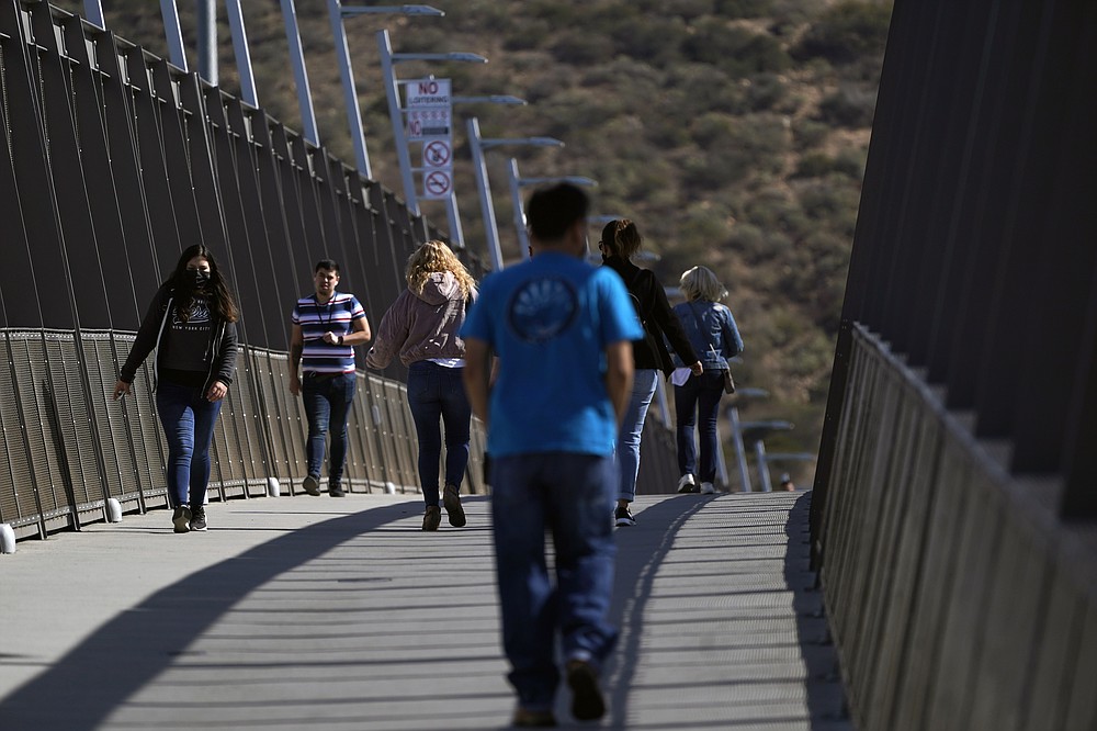 People walk on a bridge at the San Ysidro Port of Entry, connecting Tijuana, Mexico, to the United States, Wednesday, Oct. 13, 2021, in San Diego. Beleaguered business owners and families separated by COVID-19 restrictions rejoiced Wednesday after the U.S. said it will reopen its land borders to nonessential travel next month, ending a 19-month freeze. (AP Photo/Gregory Bull)