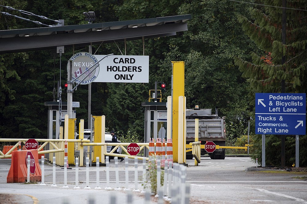 A U.S. Customs and Border Protection officer working at the Point Roberts-Boundary Bay border crossing, in Point Roberts, Wash., is seen from Delta, British Columbia, on Wednesday, Oct. 13, 2021. Point Roberts sits on a peninsula and is only accessible by land by travelling through Canada. Beleaguered business owners and families separated by COVID-19 restrictions rejoiced Wednesday after the U.S. said it will reopen its land borders to nonessential travel next month, ending a 19-month freeze. (Darryl Dyck/The Canadian Press via AP)