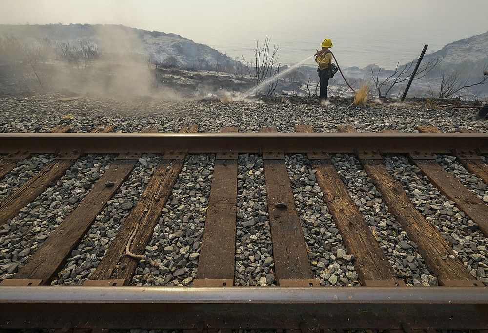 County of Santa Barbara Fire Department firefighters extinguish a roadside fire next to train tracks off of the U.S. 101 highway Wednesday, Oct. 13, 2021, in Goleta, Calif. A wildfire raging through Southern California coastal mountains threatened ranches and rural homes and kept a major highway shut down Wednesday as the fire-scarred state faced a new round of dry winds that raise risk of flames. The Alisal Fire covered more than 22 square miles (57 square kilometers) in the Santa Ynez Mountains west of Santa Barbara. (AP Photo/Ringo H.W. Chiu)