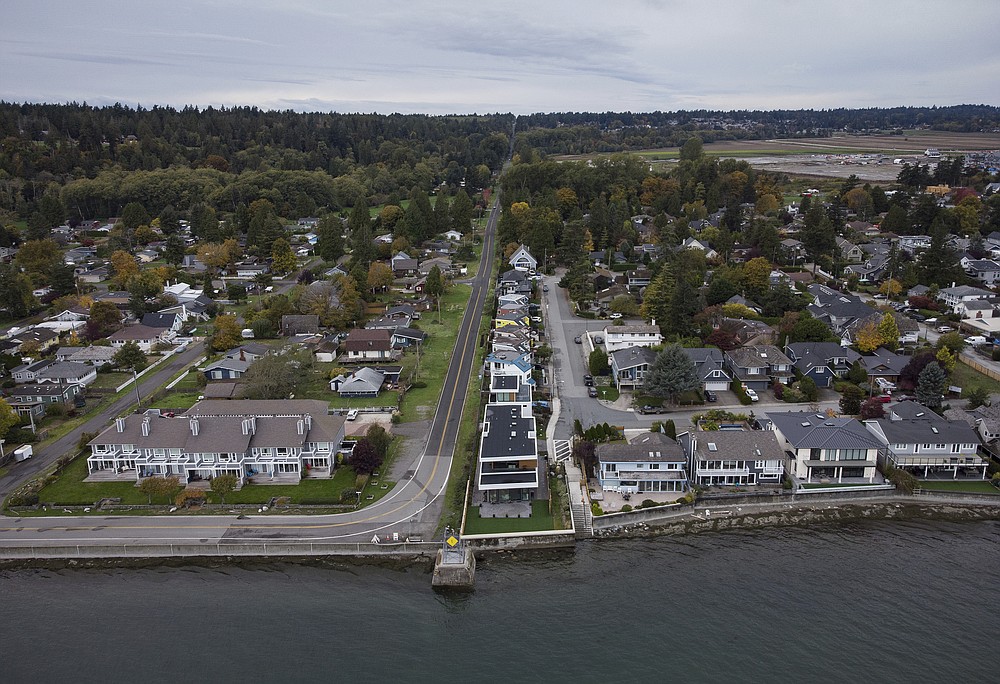 Homes in Delta, British Columbia, left, and Point Roberts, Wash., right, are separated by the Canada-U.S. border which is just north of Roosevelt Way in Point Roberts, as seen in an aerial view on Wednesday, Oct. 13, 2021. Point Roberts sits on a peninsula and is only accessible by land by travelling through Canada. Beleaguered business owners and families separated by COVID-19 restrictions rejoiced Wednesday after the U.S. said it will reopen its land borders to nonessential travel next month, ending a 19-month freeze. (Darryl Dyck/The Canadian Press via AP)