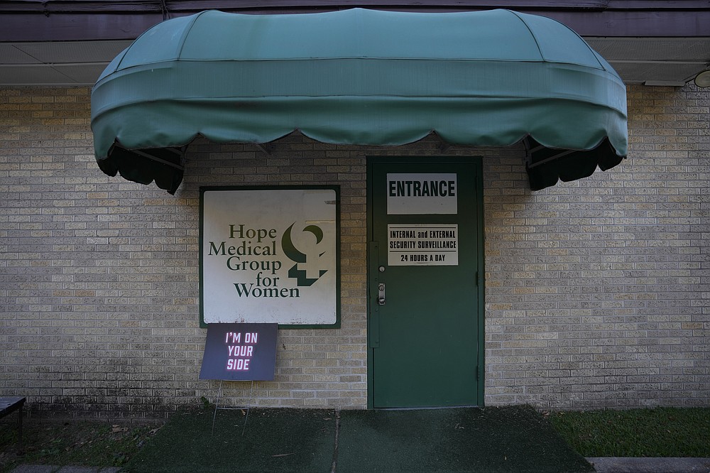 A sign supporting women seeking abortions rests beside the clinic's side door, where all visitors must pass through a security vestibule before being allowed in, Saturday, Oct. 9, 2021, at Hope Medical Group for Women in Shreveport, La. The nation's most restrictive abortion law is driving many women from Texas to seek services in neighboring states. The abortion clinic in Shreveport is among the clinics being inundated. (AP Photo/Rebecca Blackwell)