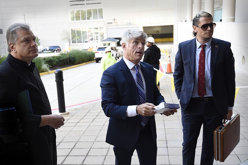 FILE - Fr. Paul Kalchik, left, St. Michael&#x2019;s Media founder and CEO Michael Voris, center, and Milo Yiannopoulos talk with a court officer before entering the federal courthouse, Sept. 30, 2021 in Baltimore. A federal judge has blocked Baltimore city officials from banning the conservative Roman Catholic media outlet from holding a prayer rally at a city-owned pavilion during a U.S. bishops&#x2019; meeting next month. U.S. District Judge Ellen Hollander ruled late Tuesday, Oct. 13, 2021 that St. Michael&#x2019;s Media is likely to succeed on its claims that the city discriminated against it on the basis of its political views and violated its First Amendment free speech rights. (AP Photo/Gail Burton, file)