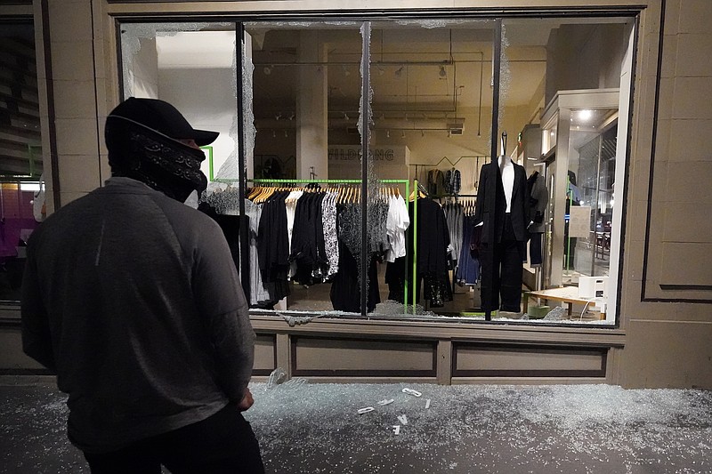 FILE - In this Nov. 4, 2020, file photo, a man stands in front of a broken display window at a retail store during protests in Portland, Ore. Police in Portland say they believe a new state law prohibits officers from directly intervening when people smash storefronts and cause mayhem. The measure passed this year prohibits the use of crowd control methods like pepper spray and rubber bullets &quot;unless use of force is otherwise authorized by statute.&quot; (AP Photo/Marcio Jose Sanchez, File)