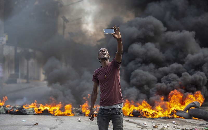 A protester takes a selfie at a burning barricade set by protesters in Port-au-Prince, Haiti, Monday, Oct. 18, 2021. Workers angry about the nation&#x2019;s lack of security went on strike in protest two days after 17 members of a U.S.-based missionary group were abducted by a violent gang. (AP Photo/Joseph Odelyn)