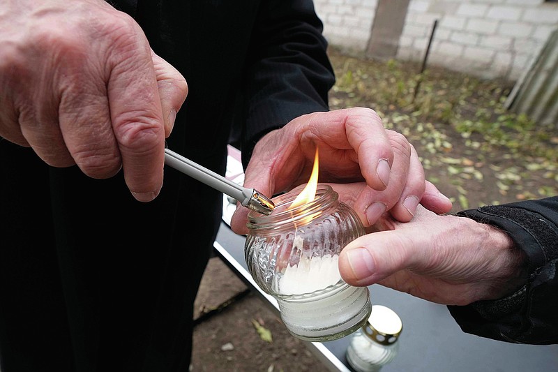 A man helps a person to light a candle to place at a new memorial paying tribute to some 60 Jews executed in the town during the Holocaust in Wojslawice, Poland, on Thursday Oct. 14, 2021. It is one of many mass grave sites to be discovered in recent years in Poland, which during World War II was occupied by Adolf Hitler&#x2019;s forces. (AP Photo/Czarek Sokolowski)