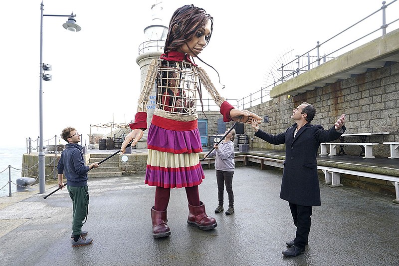 Actor Jude Law, right, looks at Little Amal, a 3.5-meter-tall puppet of a nine-year-old Syrian girl, as it arrives at Folkestone Beach, Kent, Tuesday, Oct. 19, 2021 as part of the Handspring Puppet Company's 'The Walk'. The puppet started her journey in Turkey on 27 July and has travelled nearly 8,000 km across Greece, Italy, Germany, Switzerland, Belgium and France, symbolizing millions of displaced children. (Gareth Fuller/PA via AP)