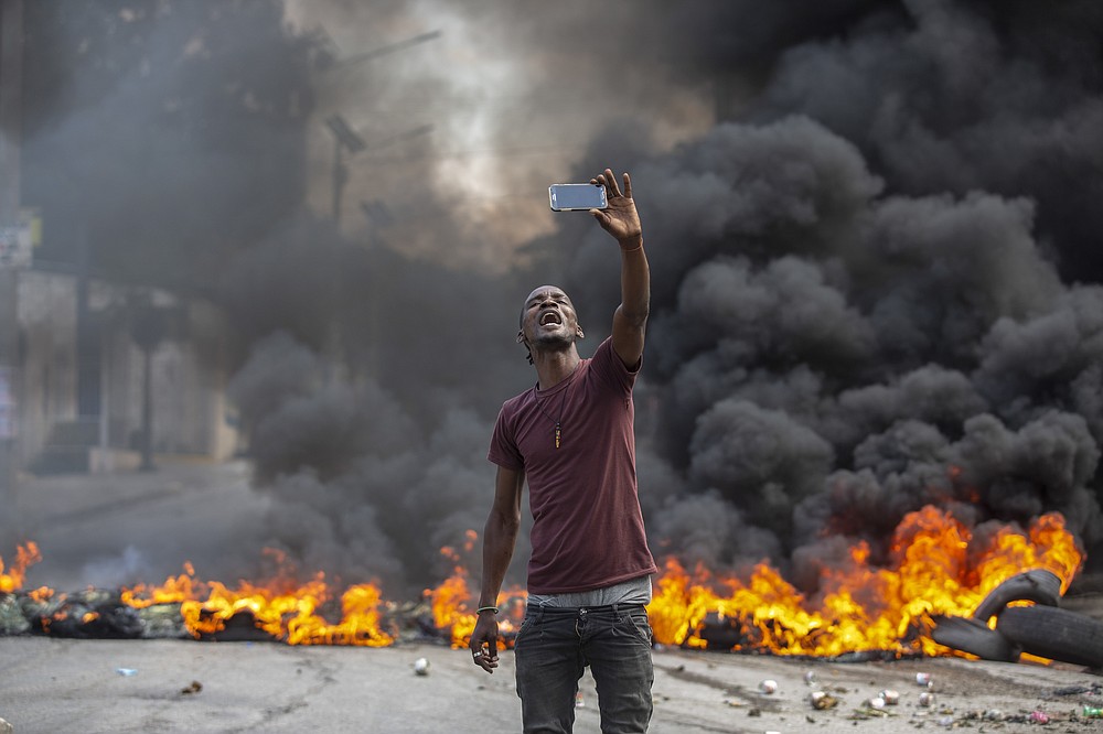 A protester takes a selfie at a burning barricade set by protesters in Port-au-Prince, Haiti, Monday, Oct. 18, 2021. Workers angry about the nation’s lack of security went on strike in protest two days after 17 members of a U.S.-based missionary group were abducted by a violent gang. (AP Photo/Joseph Odelyn)