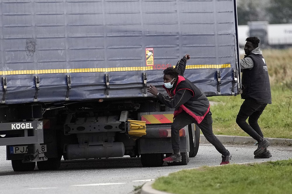 Migrants try to jump on a truck in Calais, northern France, Thursday, Oct. 14, 2021, to cross the tunnel heading to Britain. In a dangerous and potentially deadly practice, they are trying to get through the heavily policed tunnel linking the two countries by hiding on a truck. (AP Photo/Christophe Ena)