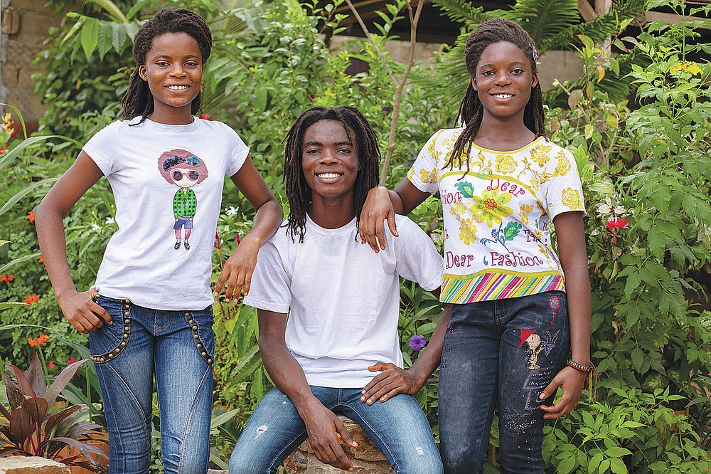 Tyrone Iras Marhguy, 17, center, poses for a photograph with his triplet sisters Nikita Hive Marhguy, left, and Amrita Sheeba Marhguy at their home in Accra, Ghana, Sunday, Oct. 10, 2021. An official at the academically elite Achimota School in Ghana told the teen he would have to cut his dreadlocks before enrolling. For Marhguy, who is a Rastafarian, cutting his dreadlocks is non-negotiable so he and his family asked the courts to intervene. (AP Photo/Nipah Dennis)