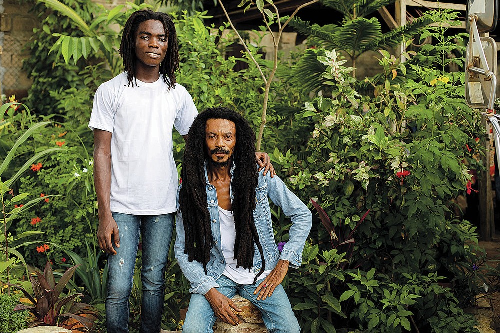 Tyrone Iras Marhguy, 17, left, poses for a photograph with his father Tereo Awareness Marhguy at their home in Accra, Ghana, Sunday, Oct. 10, 2021. An official at the academically elite Achimota School in Ghana told Tyrone he would have to cut his dreadlocks before enrolling. For Marhguy, who is a Rastafarian, cutting his dreadlocks is non-negotiable so he and his family asked the courts to intervene. (AP Photo/Nipah Dennis)