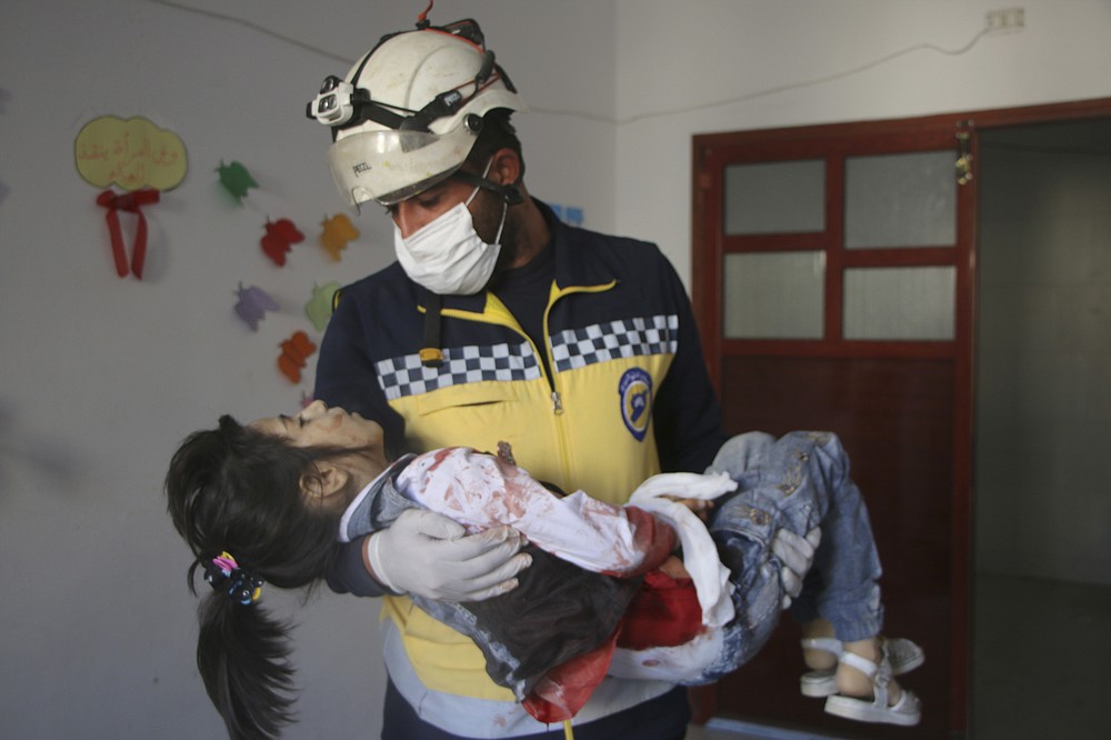 This photo provided by the Syrian Civil Defense White Helmets, which has been authenticated based on its contents and other AP reporting, shows Syrian White Helmet civil defense workers carrying a casualty, in the northern town of Ariha, in Idlib province, Syria, Wednesday, Oct. 20, 2021. Rescue workers reported several people were killed, including children and a woman, in  shelling by Syrian government forces on Ariha, in the last rebel enclave in the country's northwest. (Syrian Civil Defense White Helmets via AP)