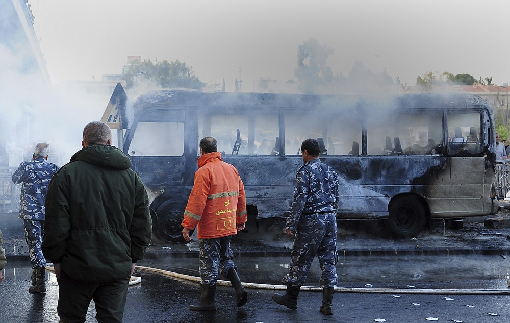 In this photo released by the Syrian official news agency SANA, Syrian firefighters and security officer check a burned bus at the site of a deadly explosion, in Damascus, Syria, Wednesday, Oct. 20, 2021. Two roadside bombs exploded near a bus carrying troops during the morning rush hour in the Syrian capital early Wednesday, killing and wounding several people, state TV reported. (SANA via AP)