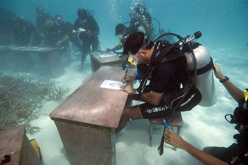 FILE - In this Saturday, Oct. 17, 2009, file photo, Maldivian President Mohammed Nasheed signs a document calling on all countries to cut down their carbon dioxide emissions ahead of a major U.N. climate change conference in December in Copenhagen, in Girifushi, about 20 minutes by speedboat from the capital Male, Maldives. Failing to limit global warming could spell a &#x201c;death sentence&#x201d; for small island developing nations like Maldives, the country's environment minister said Wednesday, Oct. 20, 2021, and added that these nations urgently needed emergency funds to mitigate the negative impacts of climate change. (AP Photo/Mohammed Seeneen, File)