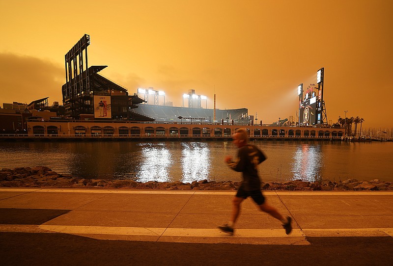 FILE - In this Wednesday, Sept. 9, 2020 file photo, a jogger runs along McCovey Cove outside Oracle Park in San Francisco, under darkened skies from wildfire smoke.Health problems tied to climate change are all getting worse, according to two reports published in the medical journal Lancet on Wednesday, Oct. 20, 2021. An unprecedented Pacific Northwest and Canadian heat wave hit this summer, which a previous study showed couldn't have happened without human-caused climate change. (AP Photo/Tony Avelar)