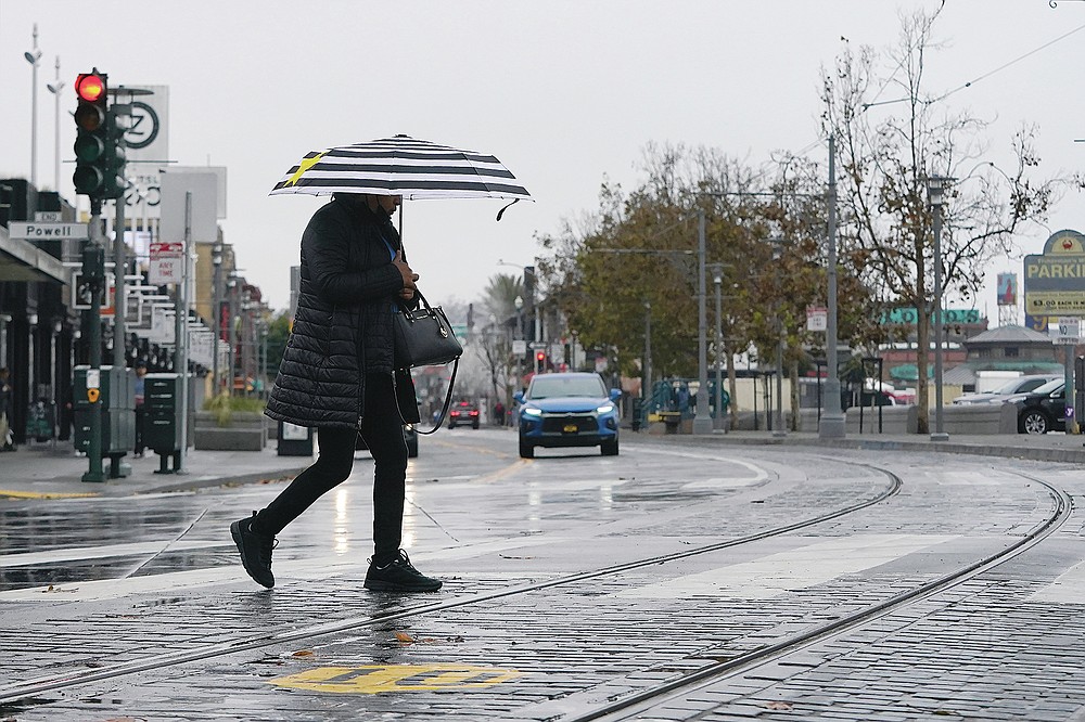 A pedestrian carries an umbrella while crossing a street at Fisherman's Wharf in San Francisco, Wednesday, Oct. 20, 2021. Showers drifted across the drought-stricken and fire-scarred landscape of Northern California on Wednesday, trailed by a series of progressively stronger storms that are expected to bring significant rain and snow into next week, forecasters said. (AP Photo/Jeff Chiu)