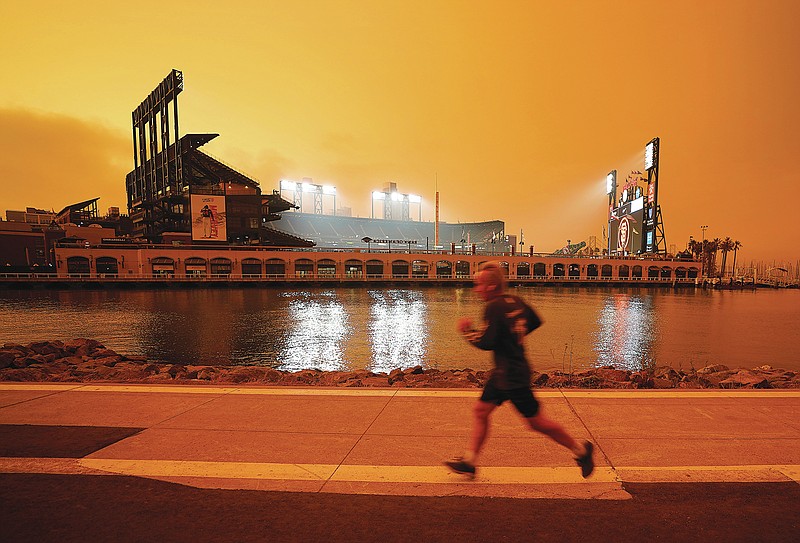 FILE - In this Wednesday, Sept. 9, 2020 file photo, a jogger runs along McCovey Cove outside Oracle Park in San Francisco, under darkened skies from wildfire smoke.Health problems tied to climate change are all getting worse, according to two reports published in the medical journal Lancet on Wednesday, Oct. 20, 2021. An unprecedented Pacific Northwest and Canadian heat wave hit this summer, which a previous study showed couldn't have happened without human-caused climate change. (AP Photo/Tony Avelar)