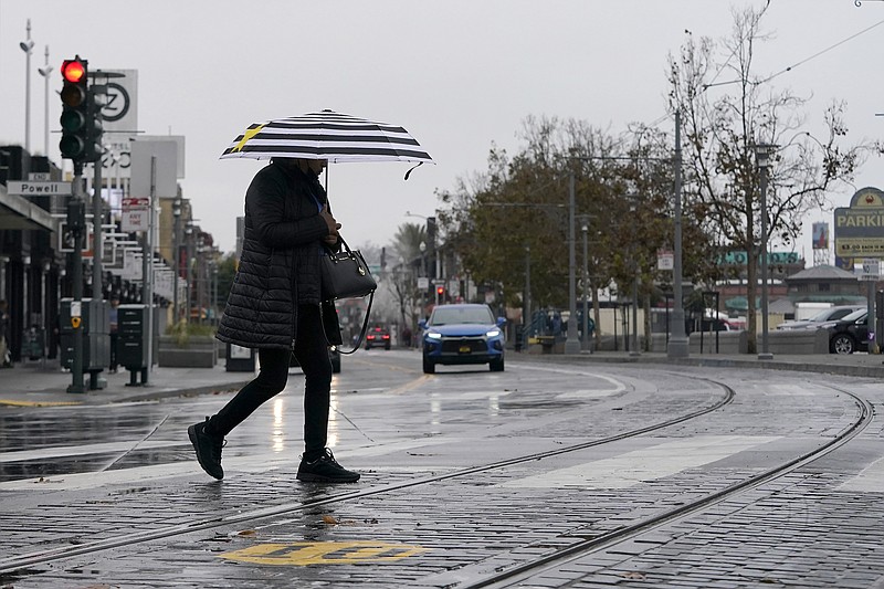 A pedestrian carries an umbrella while crossing a street at Fisherman's Wharf in San Francisco, Wednesday, Oct. 20, 2021. Showers drifted across the drought-stricken and fire-scarred landscape of Northern California on Wednesday, trailed by a series of progressively stronger storms that are expected to bring significant rain and snow into next week, forecasters said. (AP Photo/Jeff Chiu)