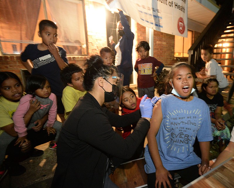 Sumina Shamory, 12, (right) reacts Friday, Oct. 22, 2021, as Ruby Lewis (center), a registered nurse with the Arkansas Department of Health, administers a covid-19 vaccination before an audience of Sumina?s family and neighbors during a vaccination event hosted by the Arkansas Coalition of Marshallese and the Arkansas Department of Health at Black Oak Apartments in Springdale. The event featured food, music and an outdoor movie night for children coupled with discussions with adults to their questions about the vaccine before a vaccination clinic began in an attempt to increase vaccinations among members of the Marshallese community. Visit nwaonline.com/211023Daily/ for today's photo gallery.
(NWA Democrat-Gazette/Andy Shupe)