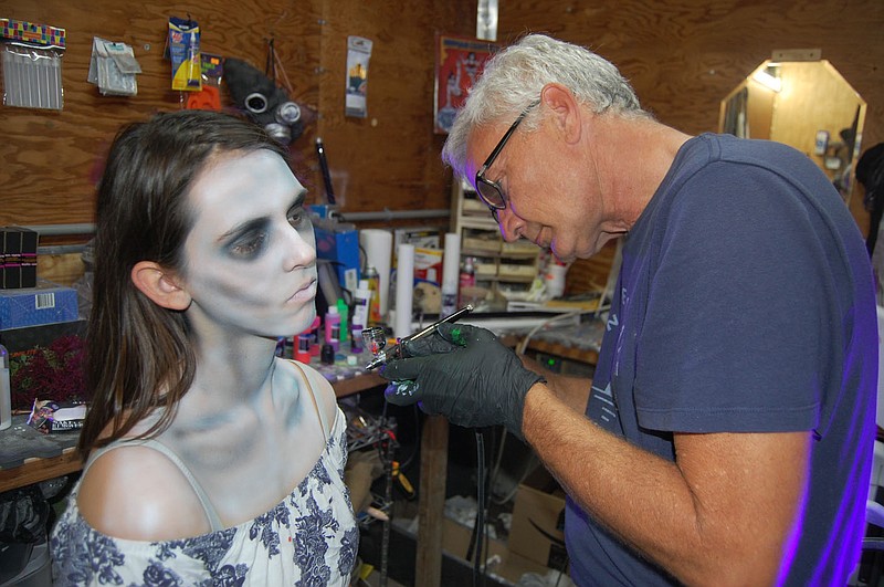 Billy Deatherage (right), of Gravette, uses an air brush to apply paint while transforming Myka Desadier, of Rogers, into a ghoulish character prior to a night of haunting at the Nightmares Haunted House on Frontage Road. The scares conclude this weekend, beginning at dusk on Friday, Saturday and Sunday nights.