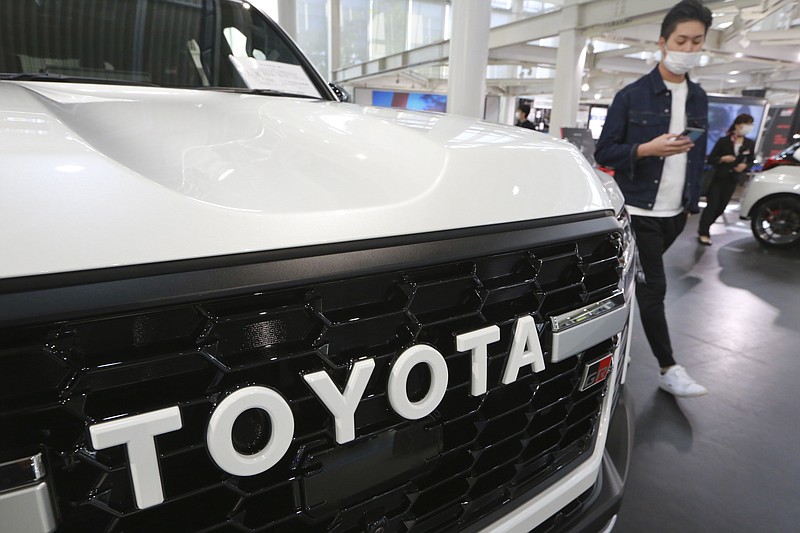 A man walks by the logo on a Toyota car at a showroom in Tokyo on Oct. 18, 2021. Toyota says it is testing hydrogen combustion engines in race cars as it works toward commercial applications of the technology. Such engines burn hydrogen as fuel instead of gasoline, much like rockets. (AP Photo/Koji Sasahara)