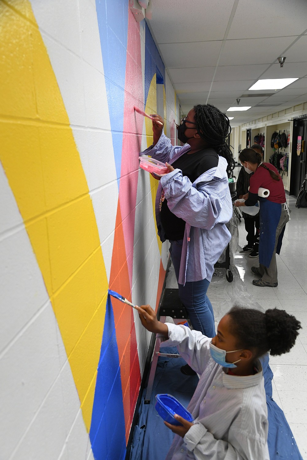 Kayden Rochelle, front, and Rayvione Clark, help Jeri Hillis, back, paint a mural at the Main Street Visual and Performing Arts Magnet School.  - Photo by Tanner Newton of The Sentinel-Record