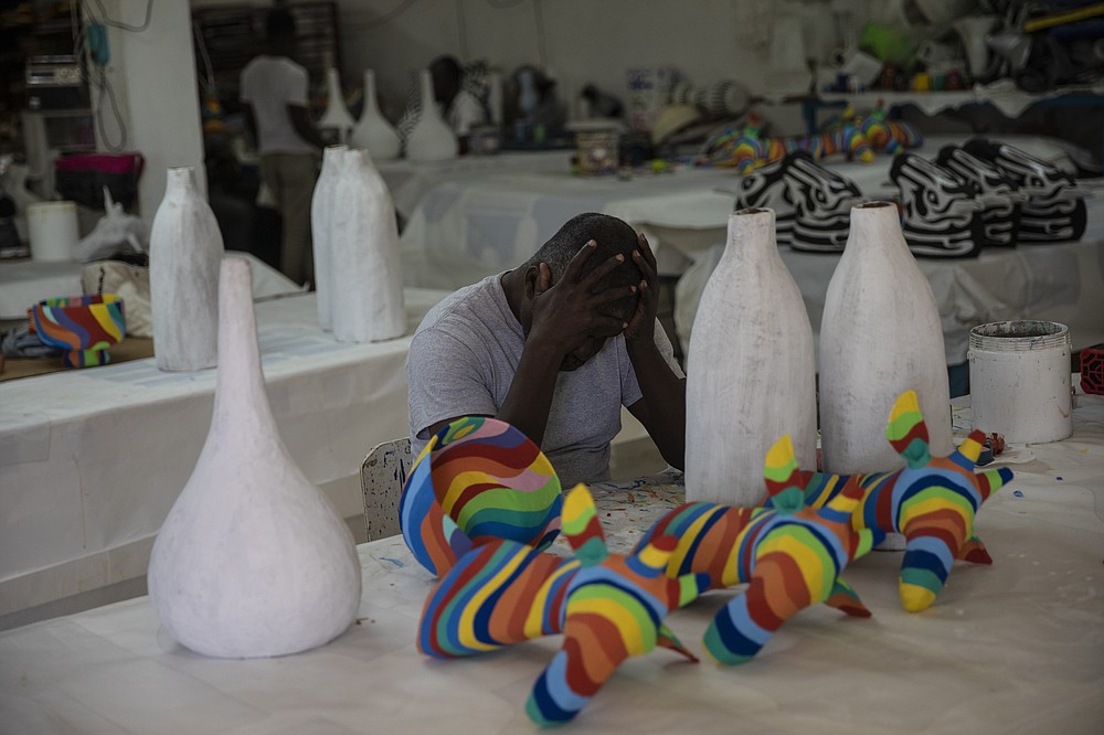 A worker takes a break while assembling art pieces at the Caribbean Craft company owned by businesswoman Magalie Dresse, in Port-au-Prince, Haiti, Tuesday, Sept. 14, 2021. Dresse's business sends about 50 containers of art to the United States each year. But before they arrive at the port, they must pass through gang-controlled areas. (AP Photo/Rodrigo Abd)