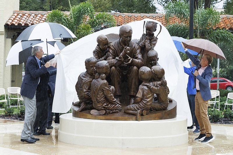 In this photo provided by Rollins College, school officials unveil a sculpture honoring alumnus and beloved children's TV host Mister Rogers, Thursday, Oct. 28, 2021, on campus in Winter Park, Fla. (Scott Cook/Rollins College via AP)