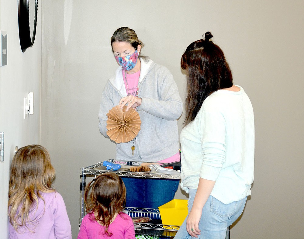 Marc Hayot/Siloam Sunday Children's Library Coordinator Mary Grayson (center), glues together a piece of paper to make the face of a scarecrow at the Siloam Springs Public Library's home schooling program. The program has been held for three years and is held weekly at 11 a.m. on Thursdays.