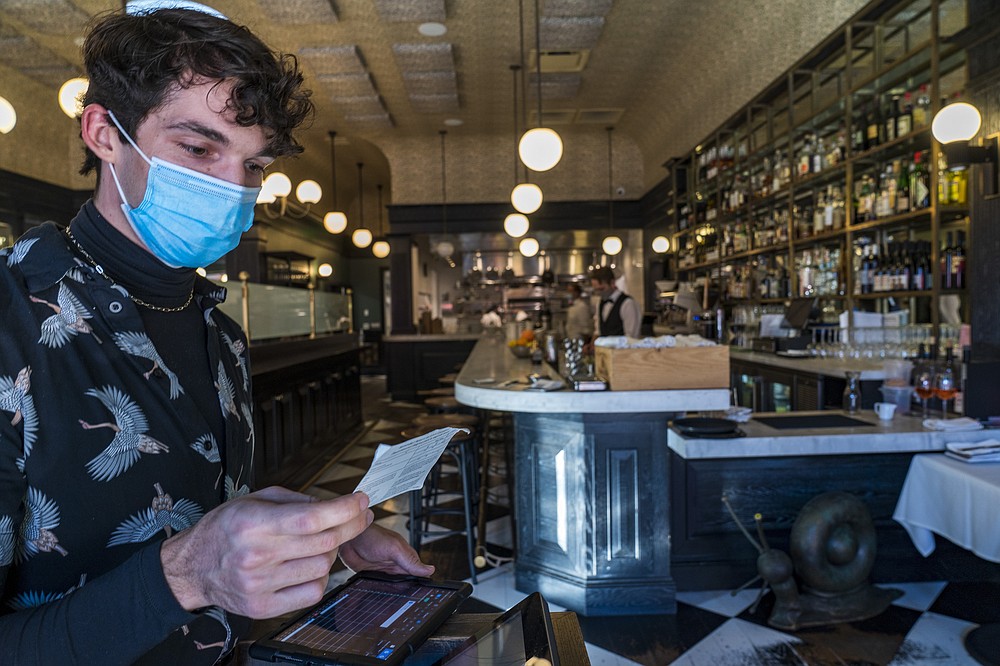 Restaurant host Joey Tyler verifies a patron's vaccination card at French restaurant Petit Trois in Los Angeles on Friday, Nov. 5, 2021. A vaccine mandate that is among the strictest in the country takes effect Monday, Nov. 8, in Los Angeles, requiring proof of shots for everyone entering a wide variety of businesses from restaurants to shopping malls and theaters to nail and hair salons. (AP Photo/Damian Dovarganes)